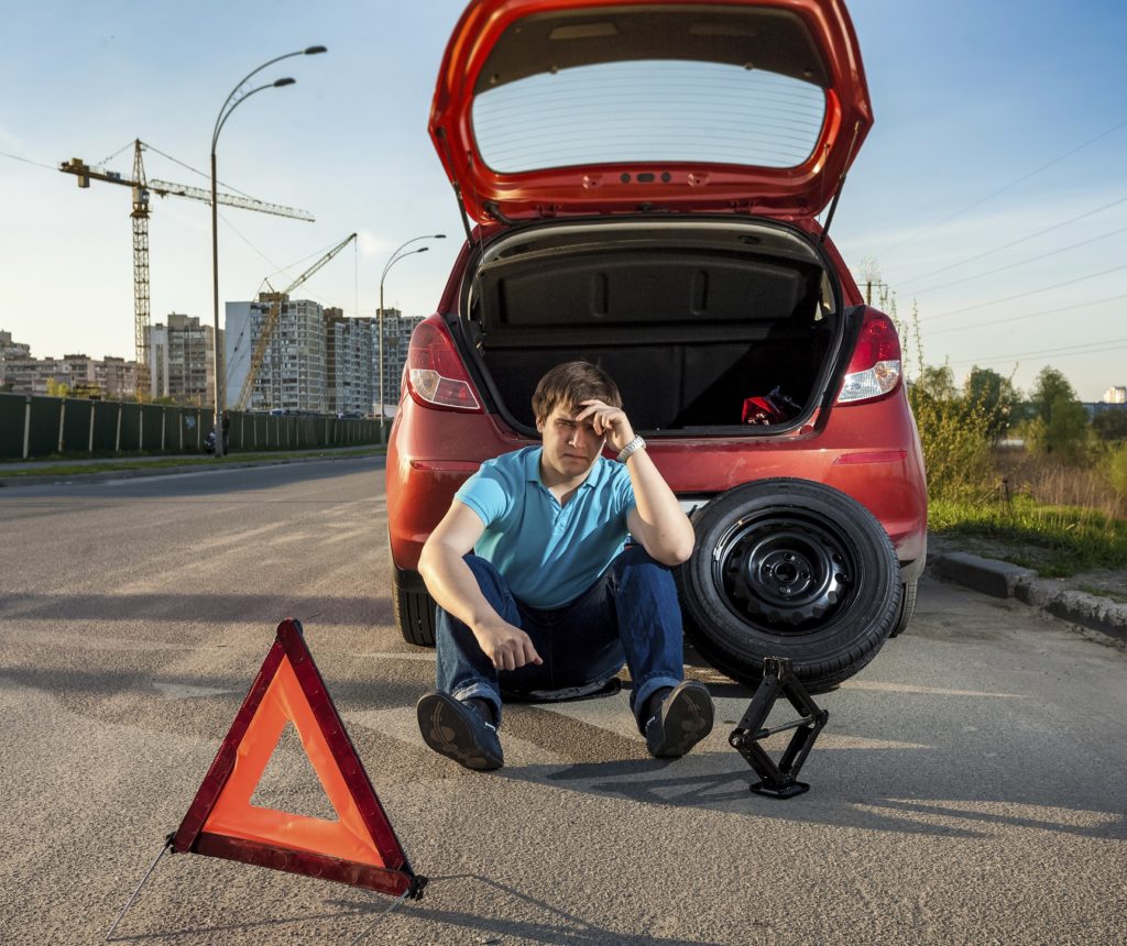 depressed man sitting near car with punctured tire